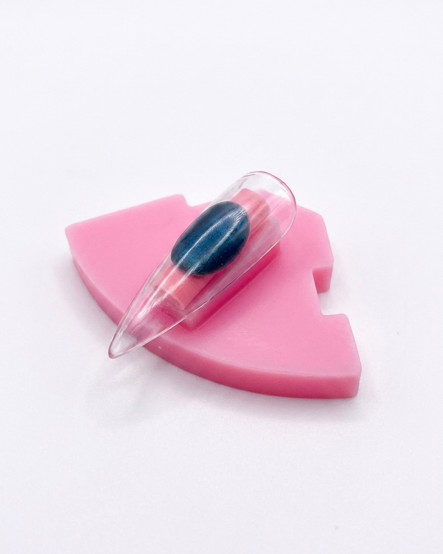 Una singola tip di unghia in plastica con finitura aurora cromata esposta in posizione verticale su un supporto rosa.