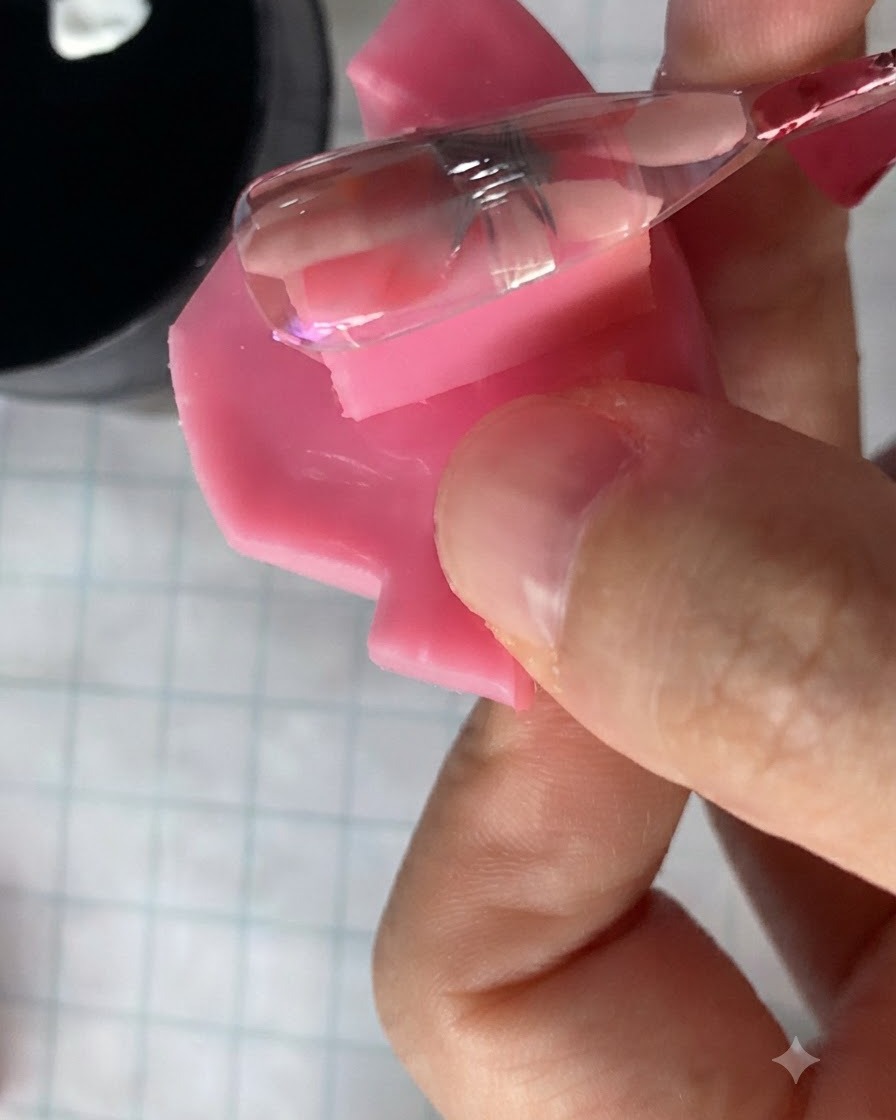 Un piccolo pennello da unghie che applica un gel rosa traslucido su un design di fiori di margherita polimerizzati su ununghia.