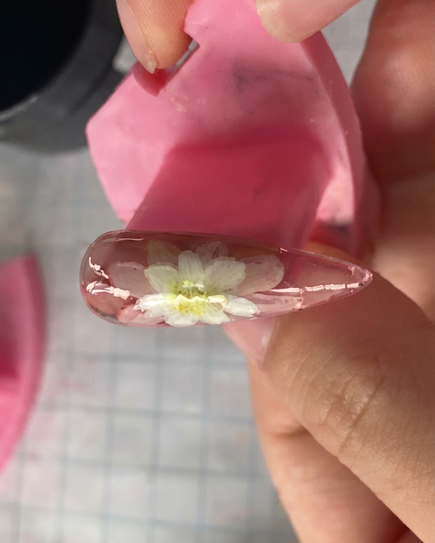 Una vista ravvicinata di un modello di unghia rosa che mostra petali di margherita bianchi stratificati dipinti sopra.