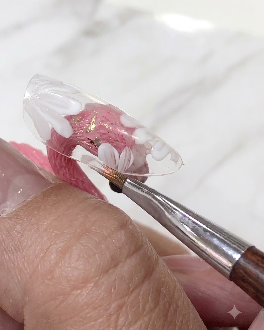 Un pennello che applica uno strato di smalto gel rosa traslucido sopra i fiori bianchi dipinti su una tip trasparente.