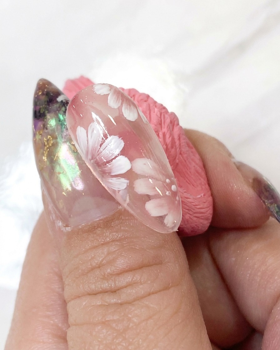 Un dotting tool che applica minuscoli punti di accento bianchi attorno al centro del fiore di un dettagliato design di nail art.