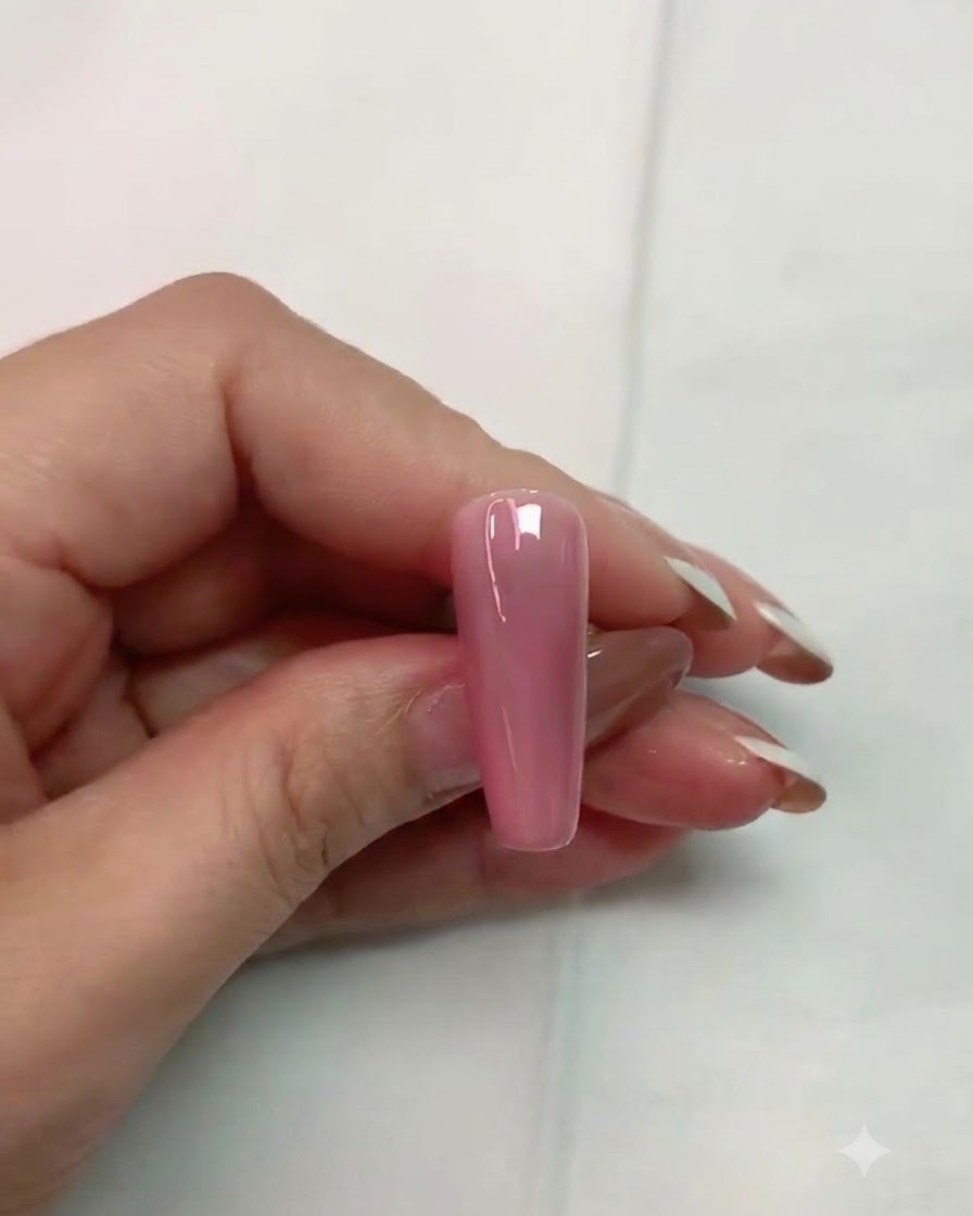 Un pennello che applica un top coat opaco trasparente sulla superficie di ununghia finta rosa lucida.