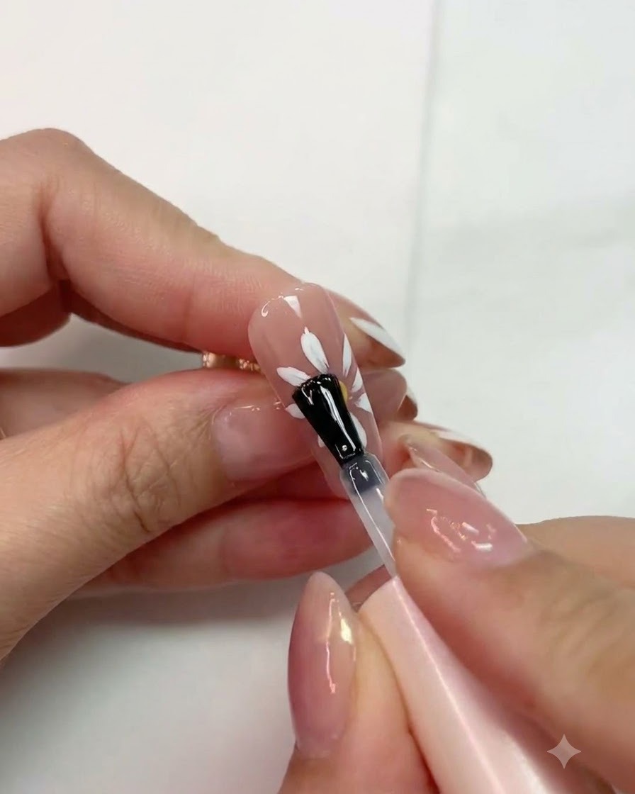 Un pennello che applica il top coat opaco su un design di margherita bianca polimerizzata su ununghia rosa.