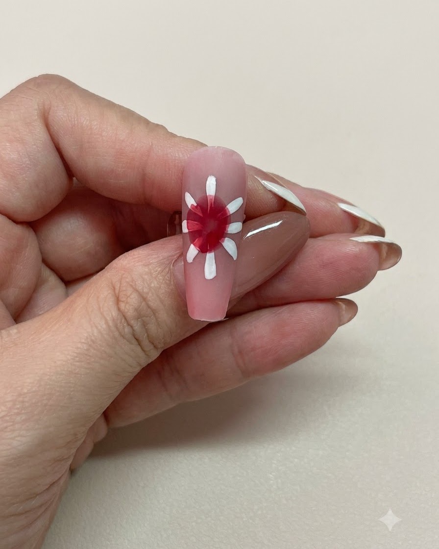 Una vista in primo piano di ununghia rosa con un centro in blooming gel rosso morbidamente diffuso circondato da petali bianchi.