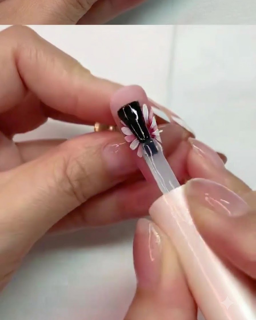 Un pennello che applica con cura il top coat opaco sui petali centrali di un design per unghie con margherita dipinta.