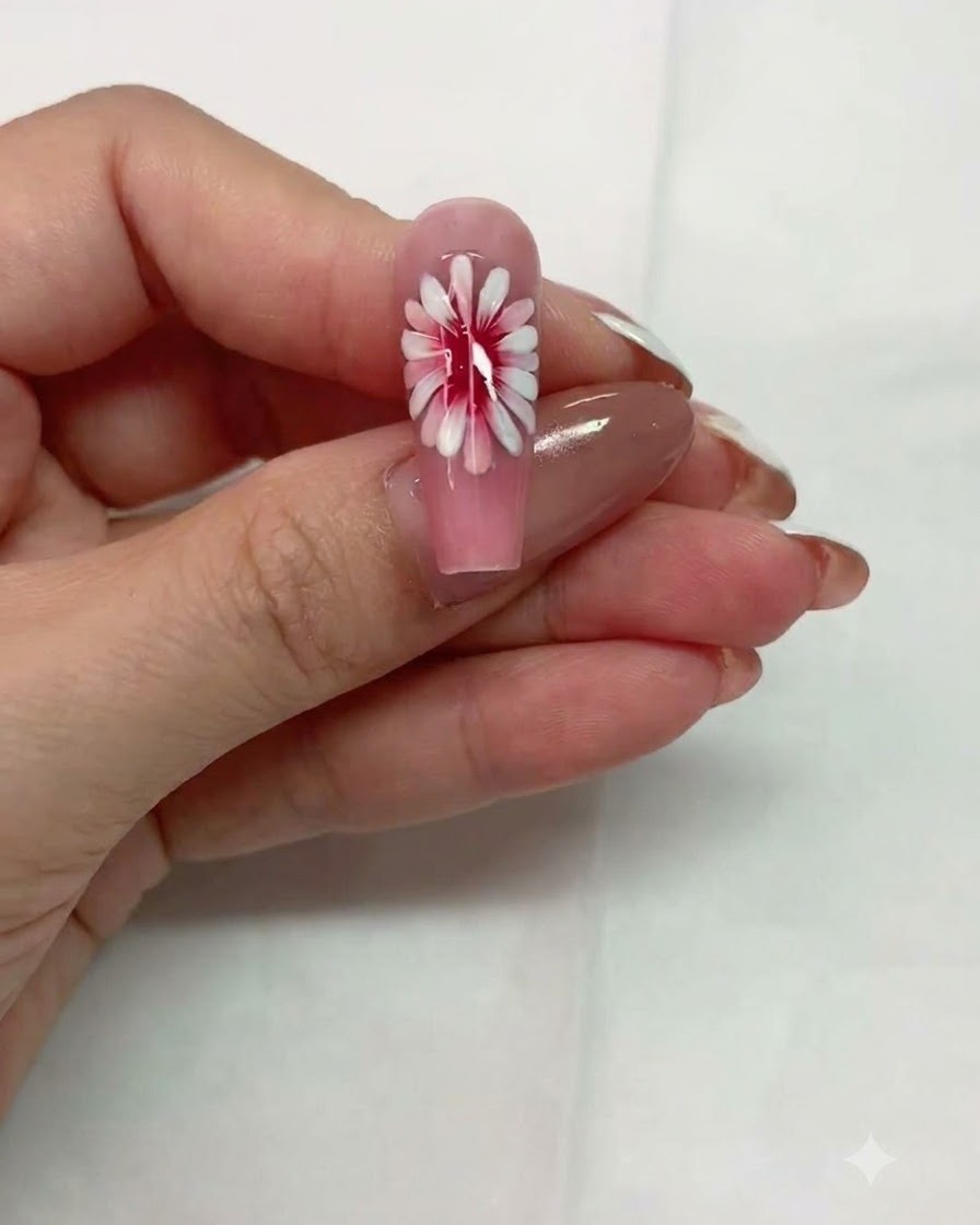 Una vista in primo piano di ununghia rosa con un design a margherita multistrato in attesa di polimerizzazione.