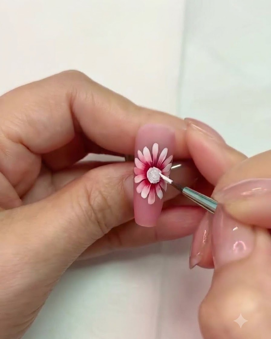 Un pennello fine che lavora vicino al centro texturizzato bianco polimerizzato della nail art a margherita.