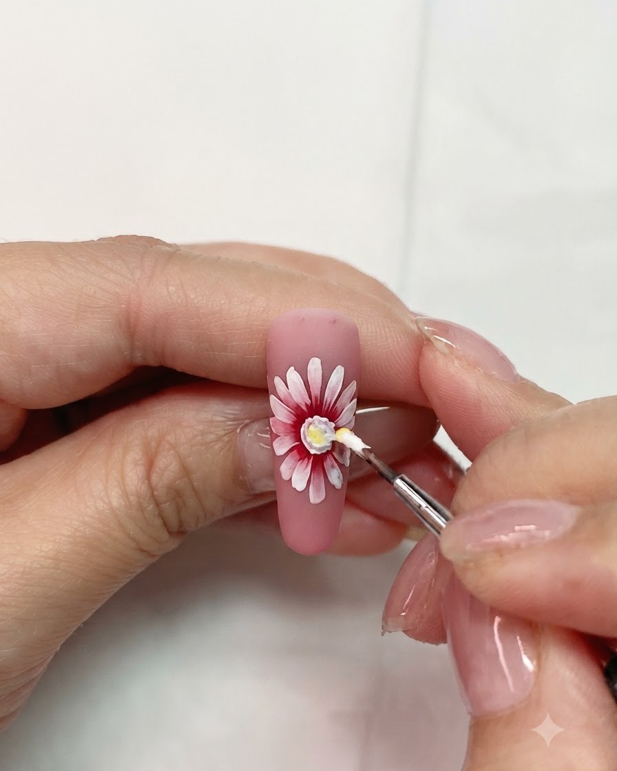 Un piccolo pennello per dettagli che applica gel giallo al centro di una nail art a margherita stratificata rosa e bianca.