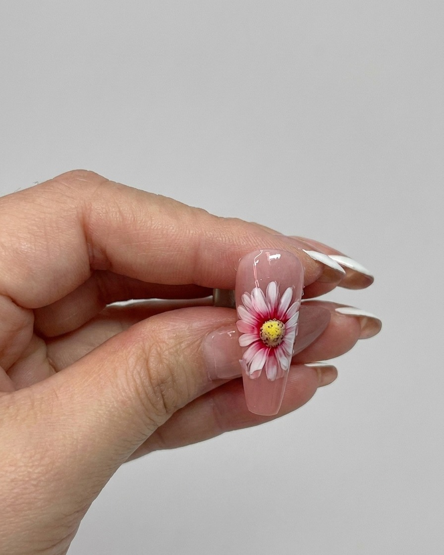 Un pennello che applica un top coat lucido su un design di unghie con margherita a doppio strato finito.