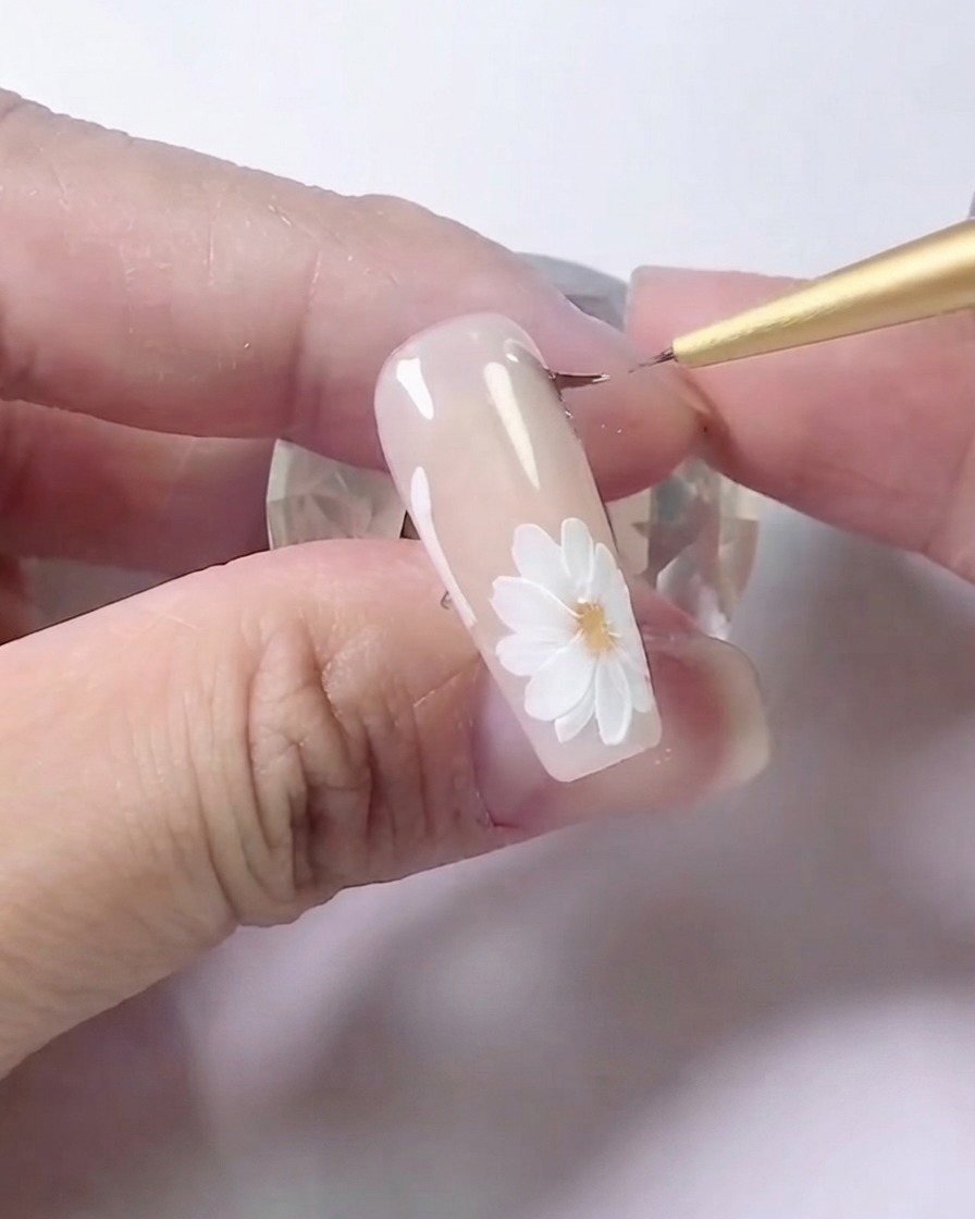 Un pennello liner che sfuma con attenzione lombra grigia lungo le linee laterali di un design di nail art floreale.