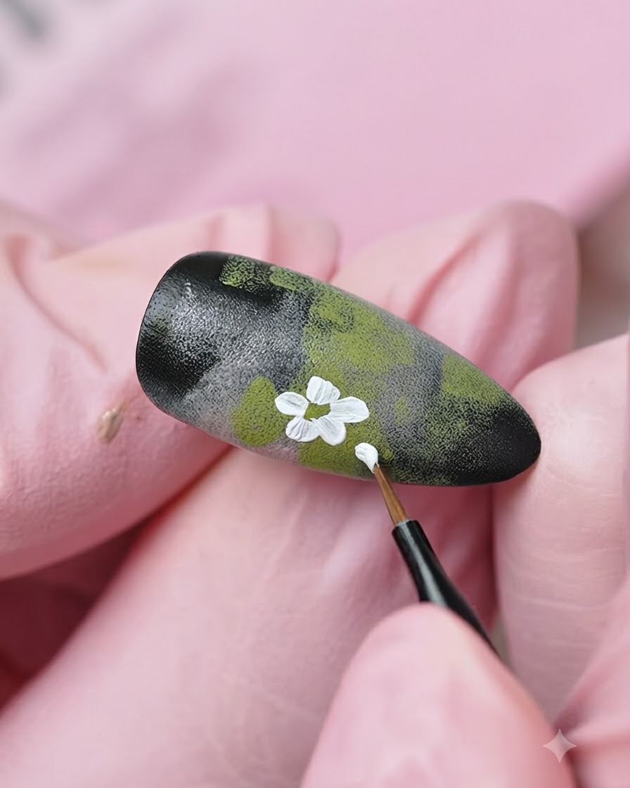 Un pennello fine a punta sottile che aggiunge ulteriori dettagli di fiori bianchi e boccioli sul design dunghia strutturato.