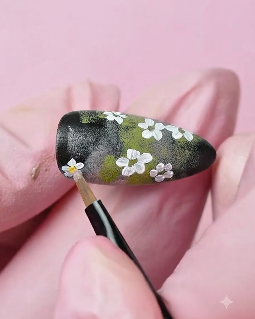 Un pennello di precisione fine che applica un punto di gel giallo al centro di un fiore bianco dipinto sullunghia.