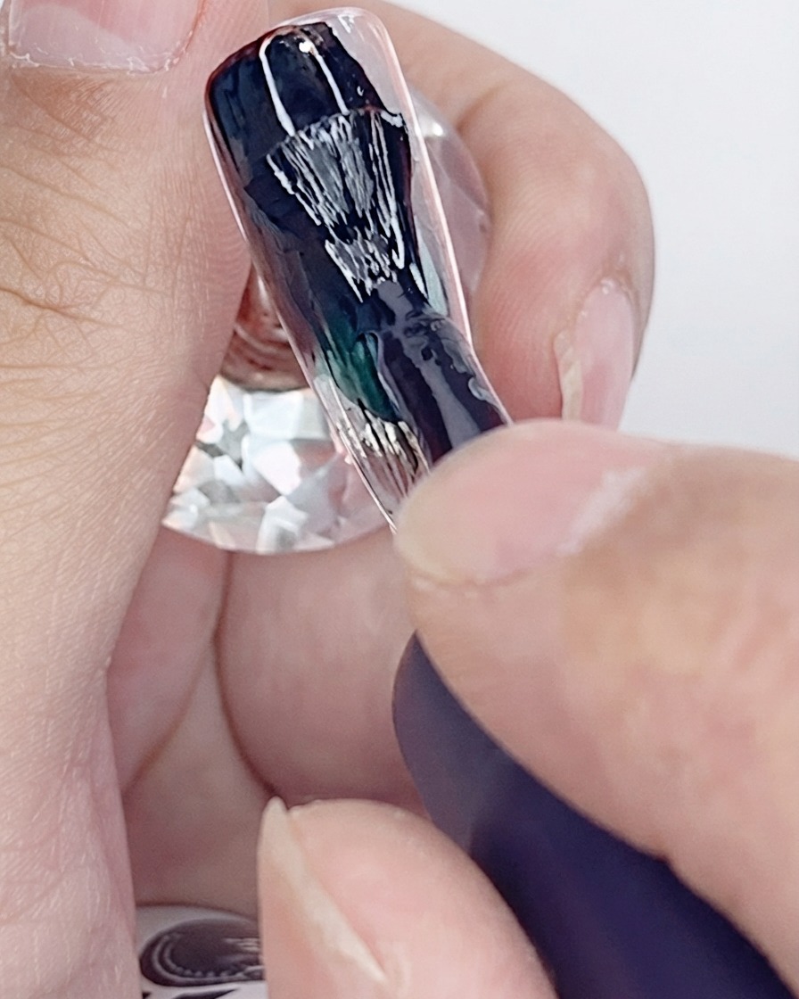 Un pennello applica la prima mano di smalto gel nero su una tip di unghia artificiale.