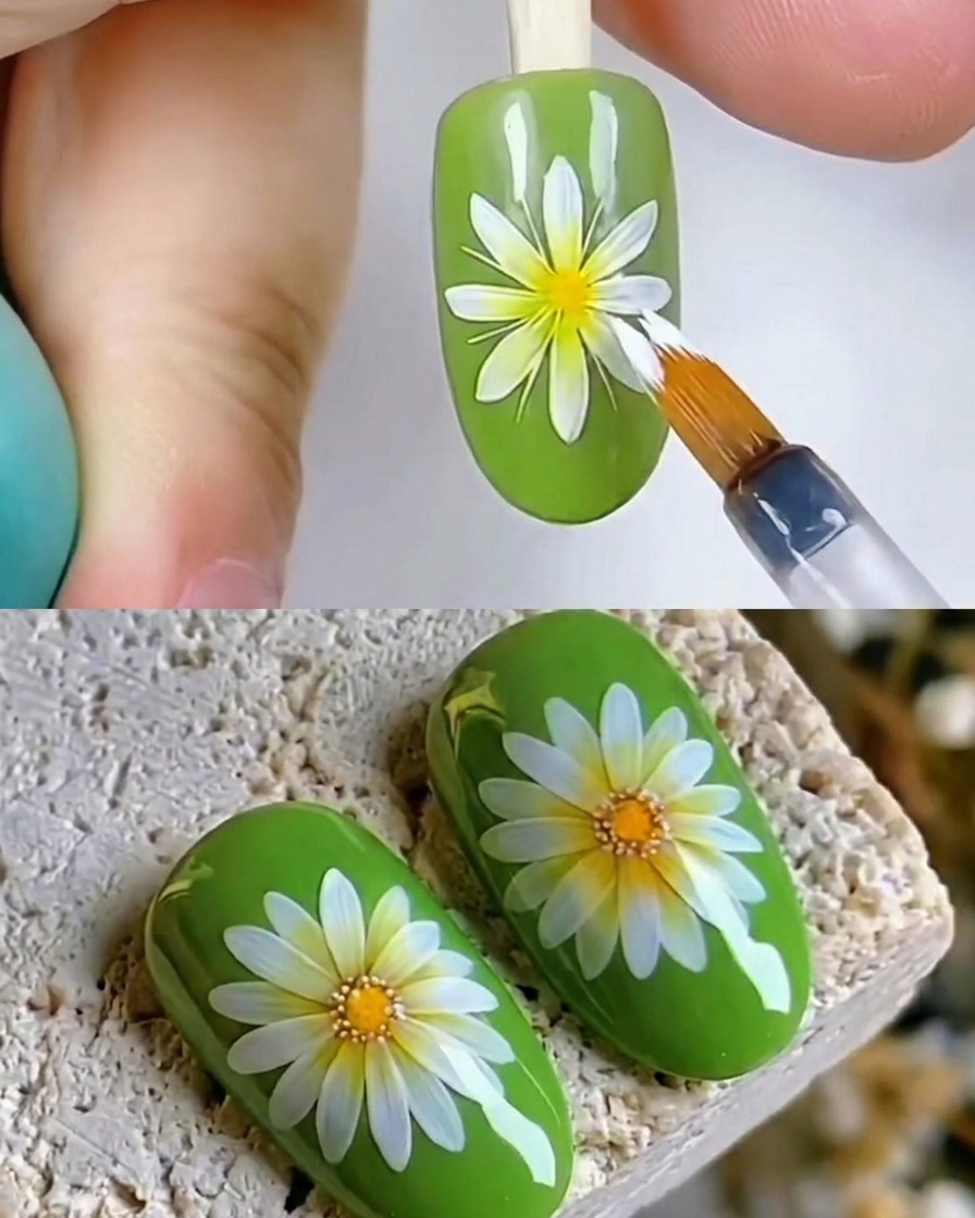 Un primo piano di un pennello che applica un top coat trasparente lucido su un design di nail art con margherita bianca su unghia verde.