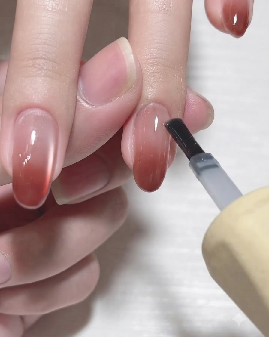 Il pennello di un flacone di gel applica un top coat lucido trasparente su ununghia sfumata completata.