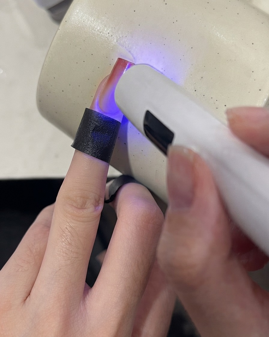 Una mini lampada UV che polimerizza la punta di ununghia sfumata con una finitura rosso vino.
