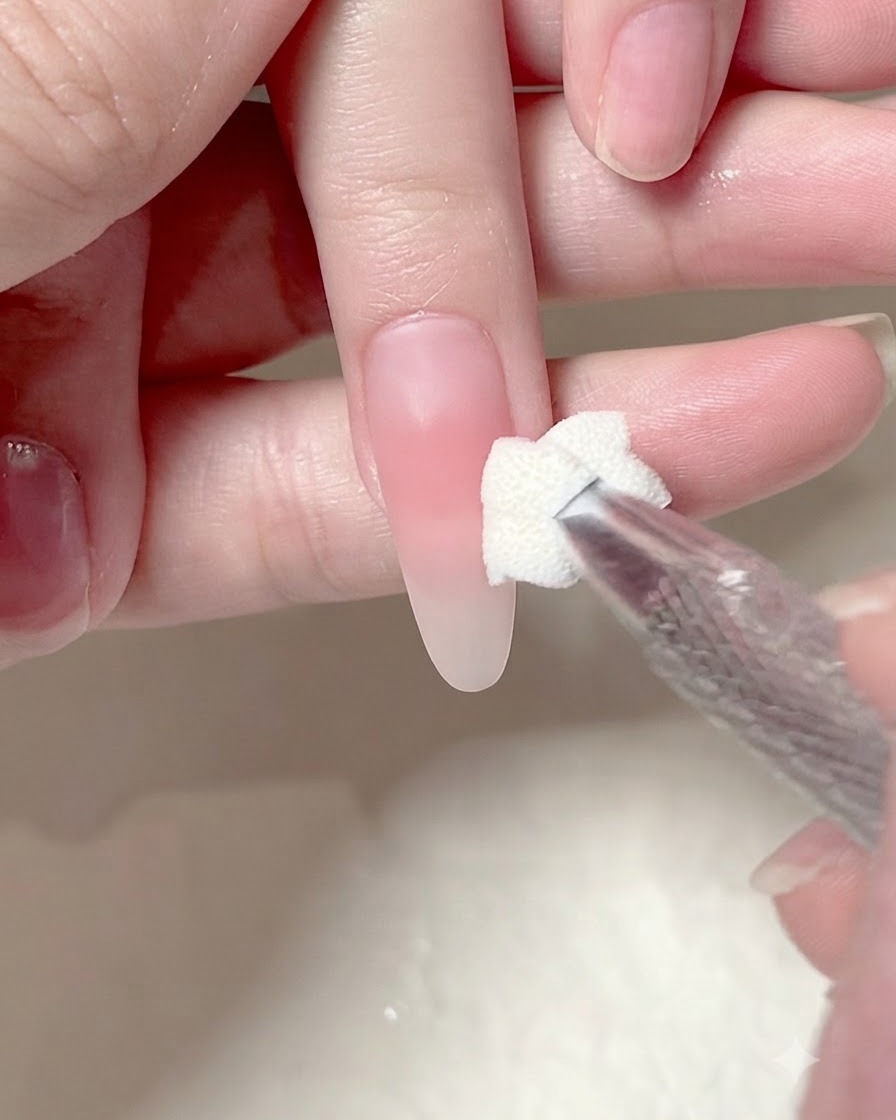 Un applicatore in spugna che tampona un secondo strato di gel rosa sul centro di ununghia manicurata.