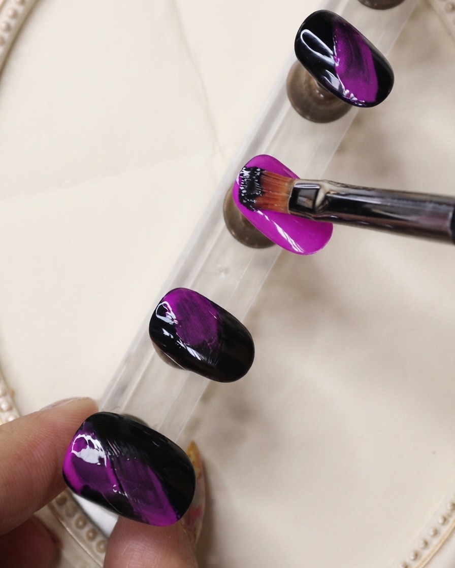 Un pennello a punta fine applica gel nero con tratti materici su ununghia viola neon.