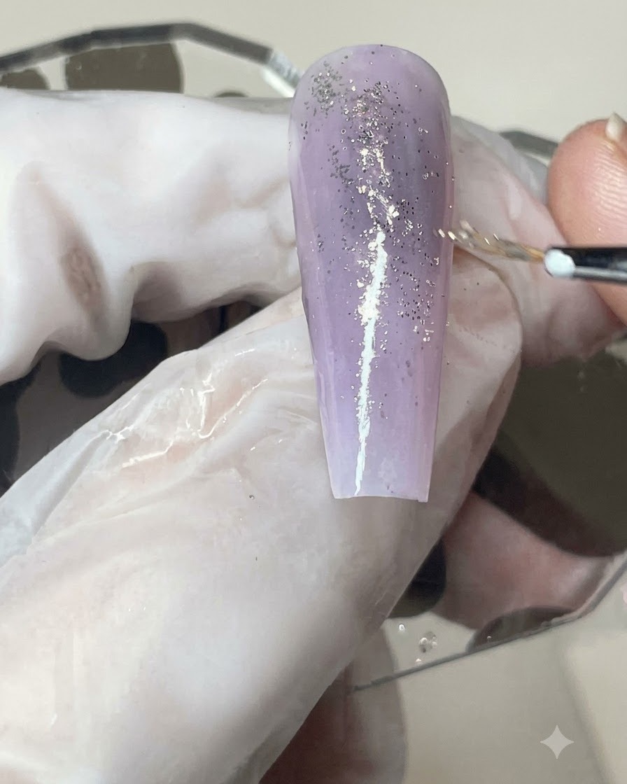 Un pennello per gel che applica uno strato liscio di top coat opaco su ununghia con sfumatura viola e glitter.