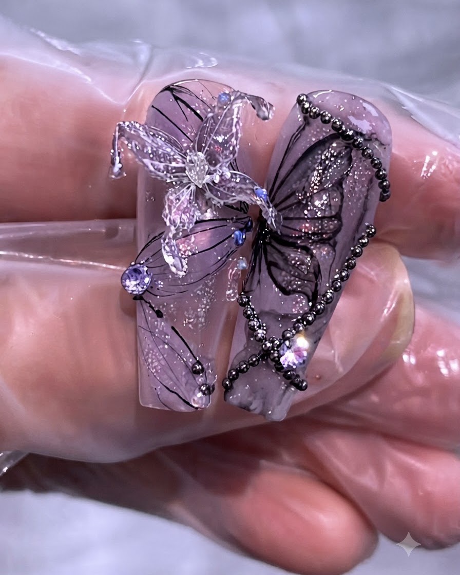 Primo piano di un set finito di nail art viola con farfalle e catene su lunghe tip trasparenti.