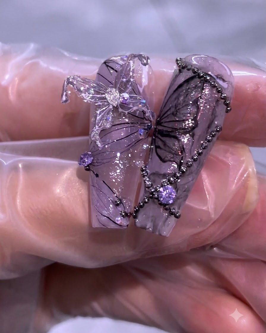 Primo piano di una nail art viola e nera completata, con dettagli di farfalle, strass e delicate linee di filo.