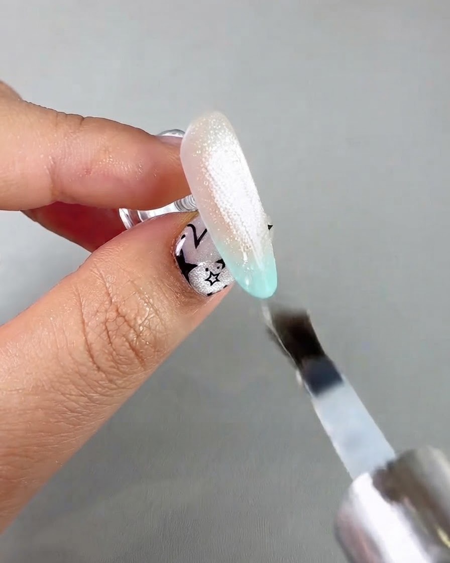 Un pennello per unghie che applica un top coat sigillante trasparente su unestensione di unghia cat eye luccicante.