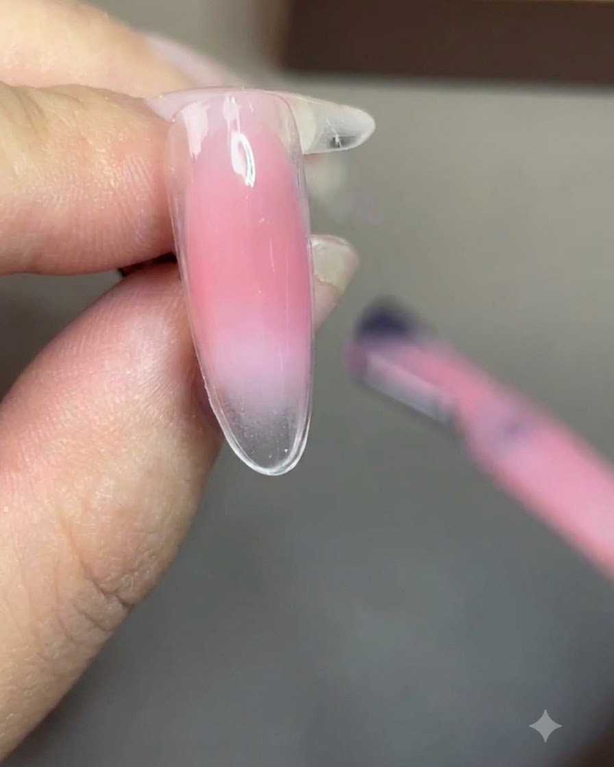Un pennello che applica uno smalto gel nude velato in modo uniforme su tutta lunghia.