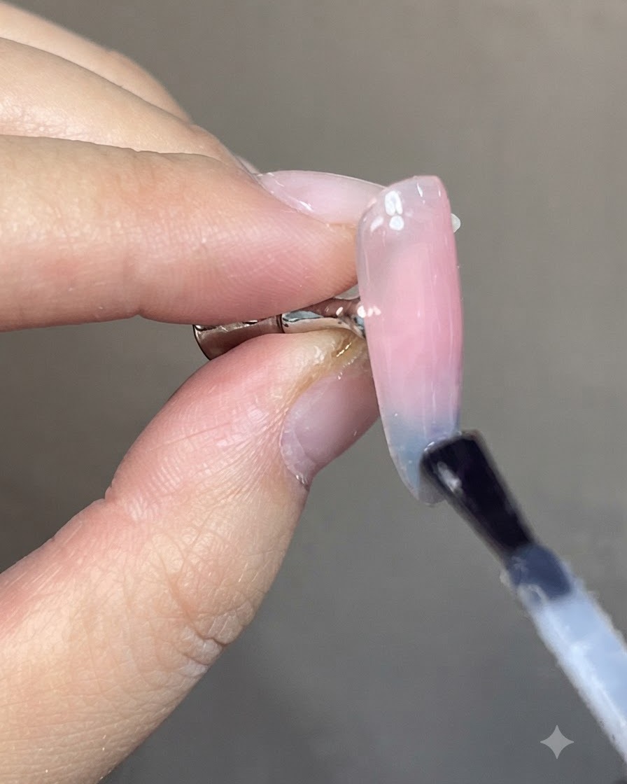 Un pennello che applica un top coat trasparente e lucido su un design per unghie sfumato cat-eye blu e rosa finito.