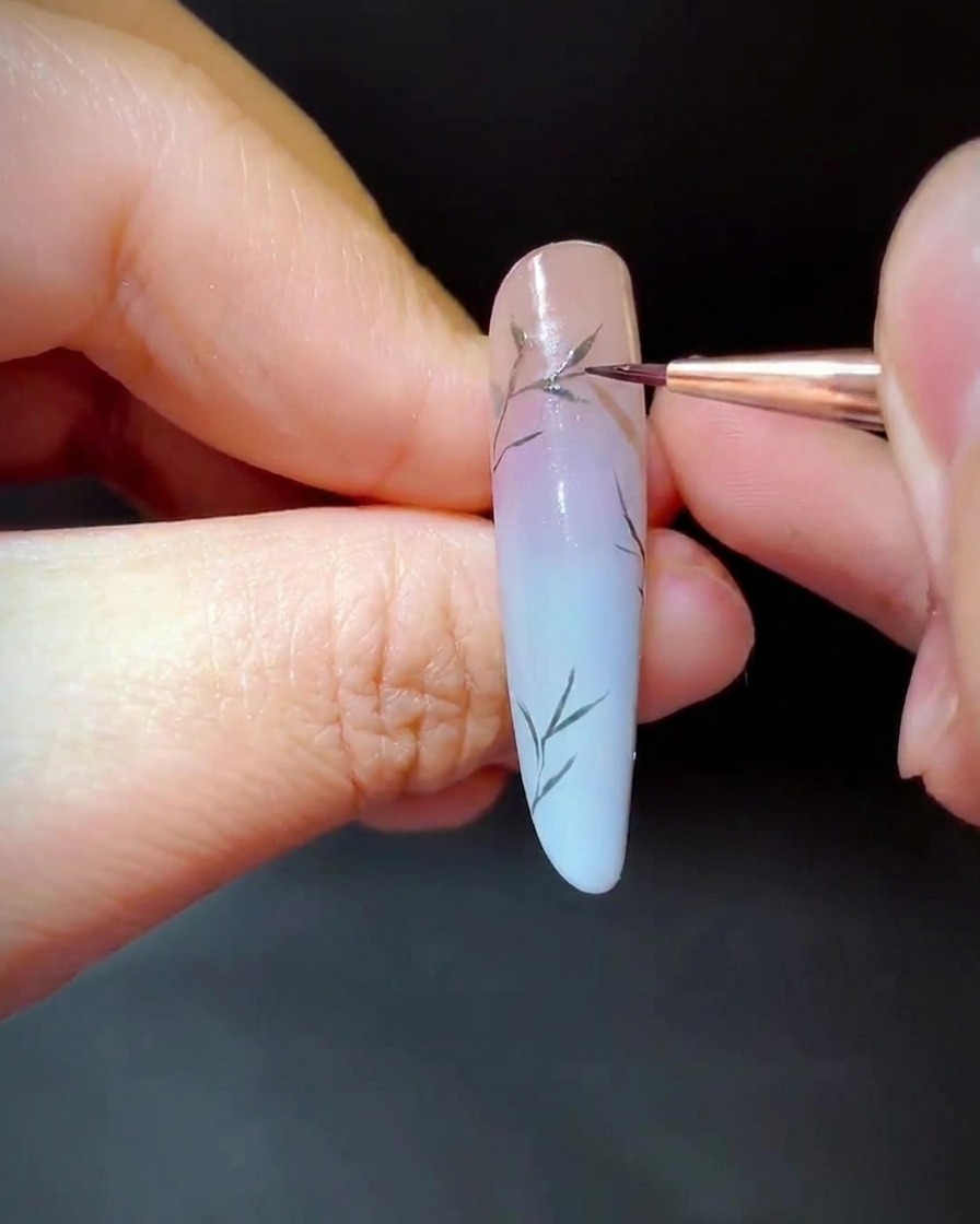 Un pennello detailer che dipinge minuscole foglie verdi lungo le sezioni inferiori dei rami dellunghia.