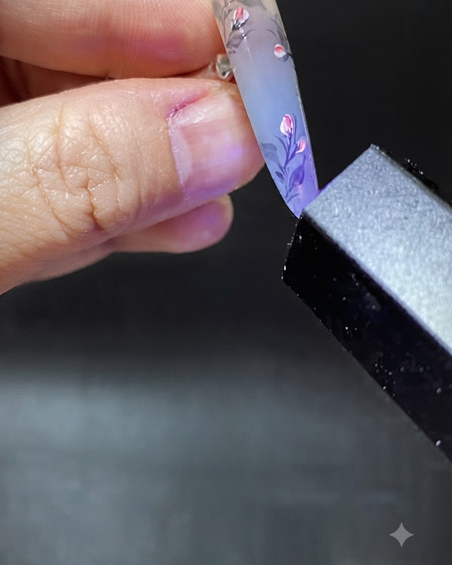 Un pennello che applica una goccia trasparente di gel di rinforzo vicino alla zona delle cuticole dellunghia decorata.