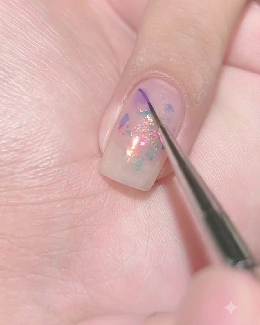 Un pennello liner sottile che deposita una minuscola goccia di gel viola scuro sulla superficie bagnata di ununghia viola trasparente.