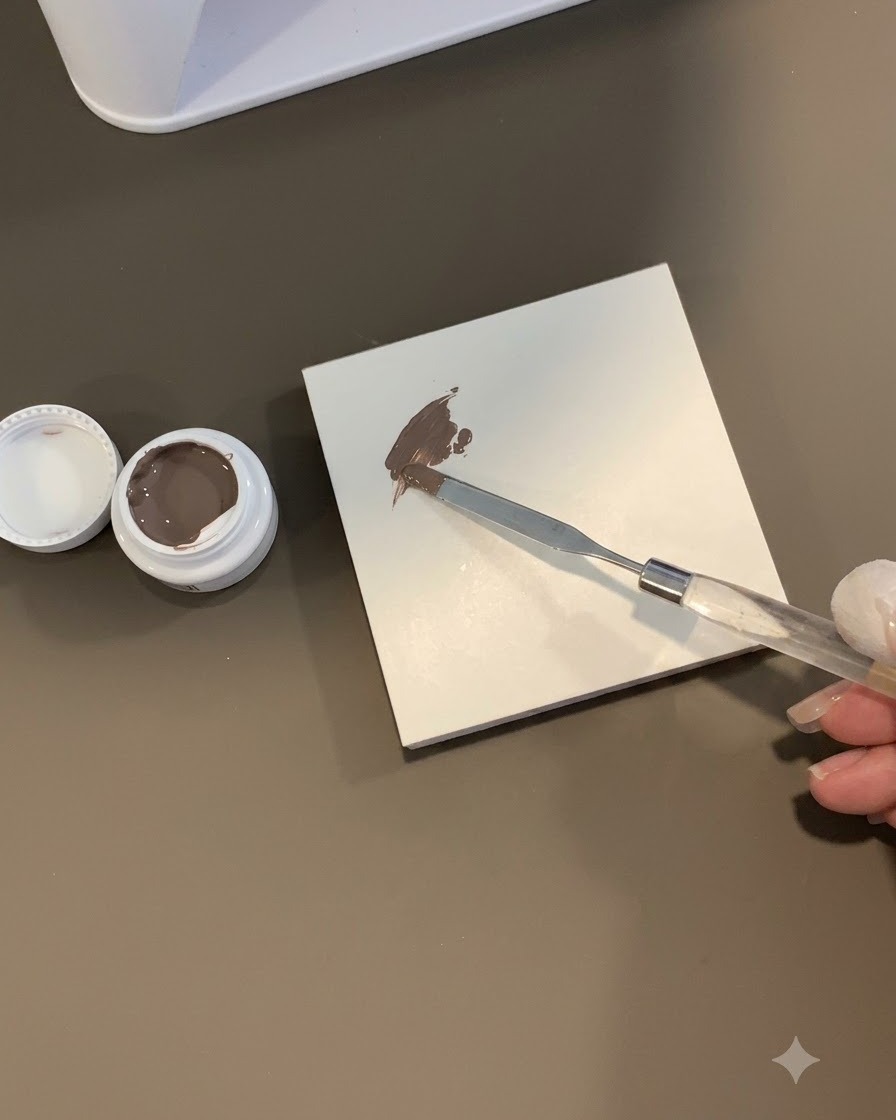 Uno strumento in spugna che tampona una chiazza di gel grigio-marrone su una superficie di piastrelle bianche.
