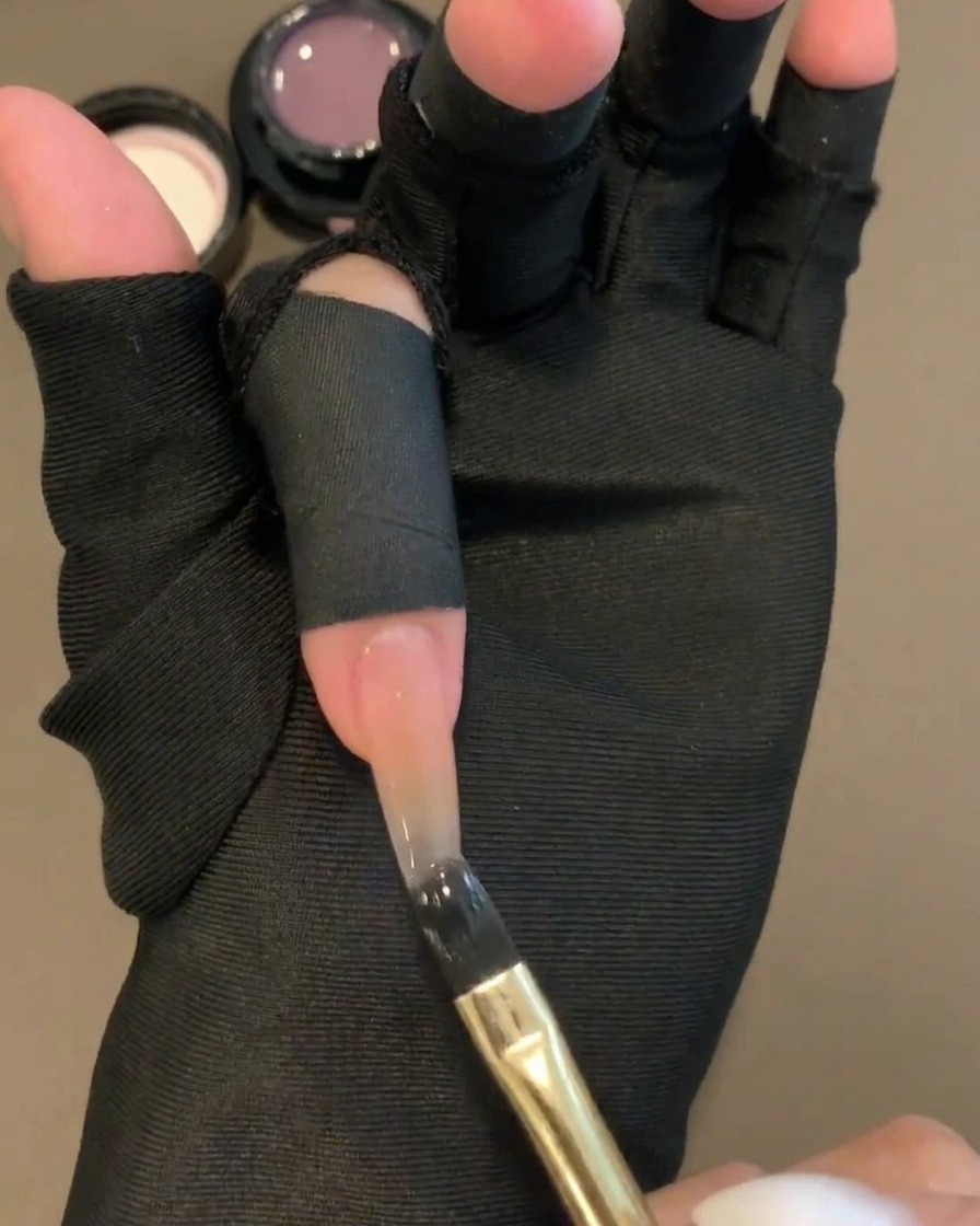 Un pennello piatto per gel che applica un gel colorato viola trasparente sulla metà superiore di ununghia con base nudo.