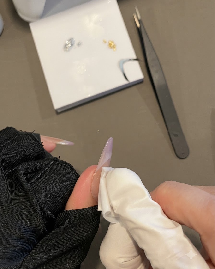 Una mano guantata che pulisce la superficie di ununghia con una velina priva di pelucchi tenendo ununghia ovale lunga.