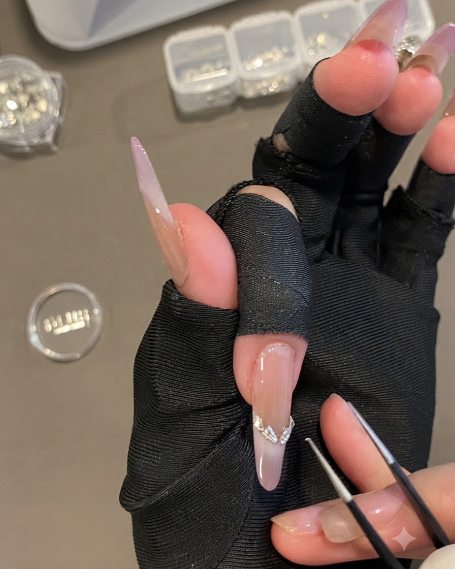 Una mano che tiene pinzette di precisione posizionando un adesivo per French tip argentato curvo su ununghia ovale lunga.