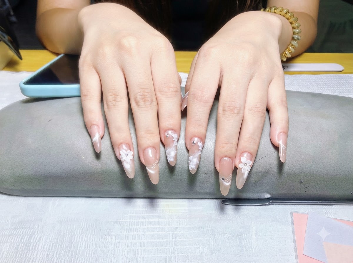 Una vista in primo piano incentrata esclusivamente sulle dita della mano sinistra, che evidenzia la finitura perlacea e le decorazioni floreali bianche.