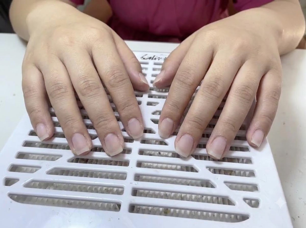 Due mani con unghie naturali nude e non smaltate posate su una superficie bianca aspiratore di polvere con fessure.