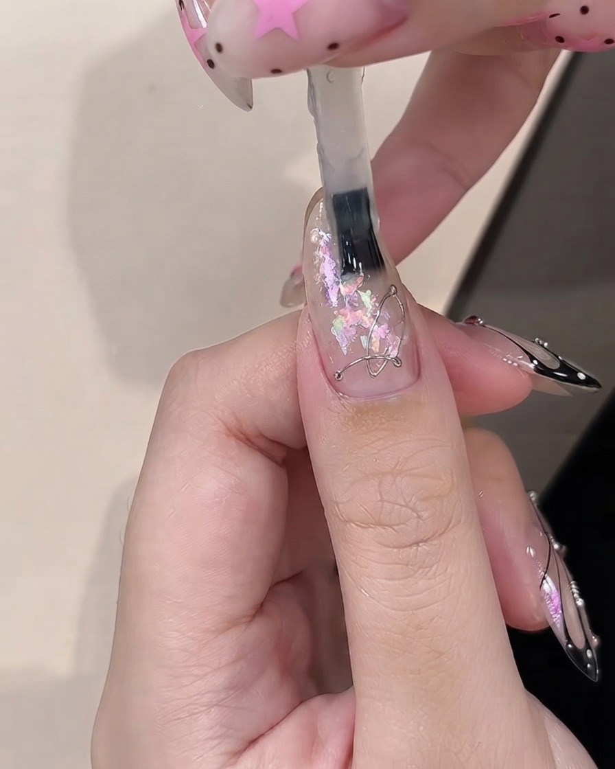 Un pennello che applica il builder gel sopra pezzi di opal decorativi incorporati su ununghia con rivestimento trasparente.
