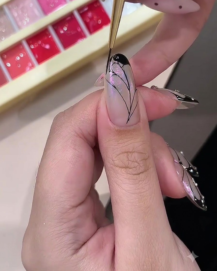 Una onicotecnica che riempie i bordi esterni di un design di ali di farfalla dipinto con gel nero opaco.