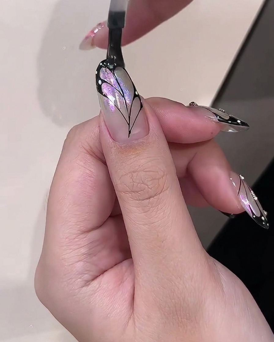 Un pennello che applica un top coat trasparente e lucido su un design finito di nail art con ali di farfalla.
