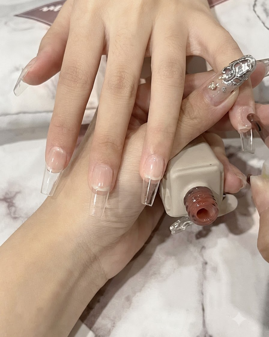 Un pennello per unghie applica un sottile strato di gel nude traslucido su una lamina ungueale naturale lunga a forma di ballerina.