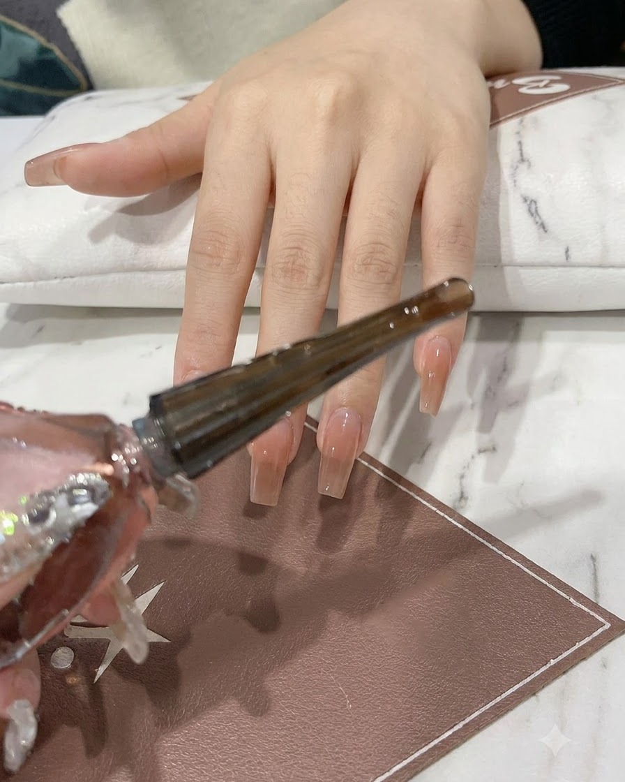 Una mano che regge una bottiglietta di gel rosa e argento brillante con il pennello applicatore estratto.
