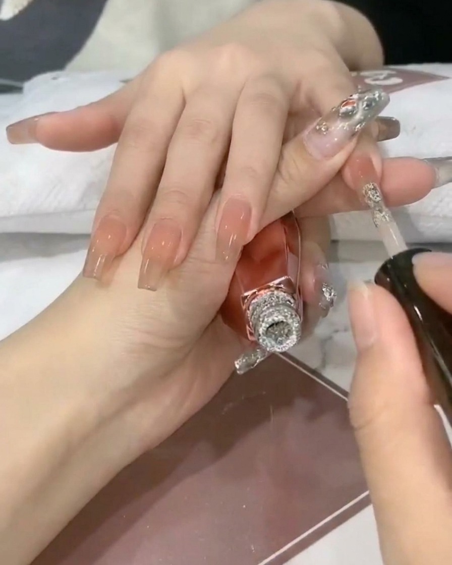 Un pennello per unghie deposita il gel glitter argento scintillante sulla punta di ununghia nude traslucida.