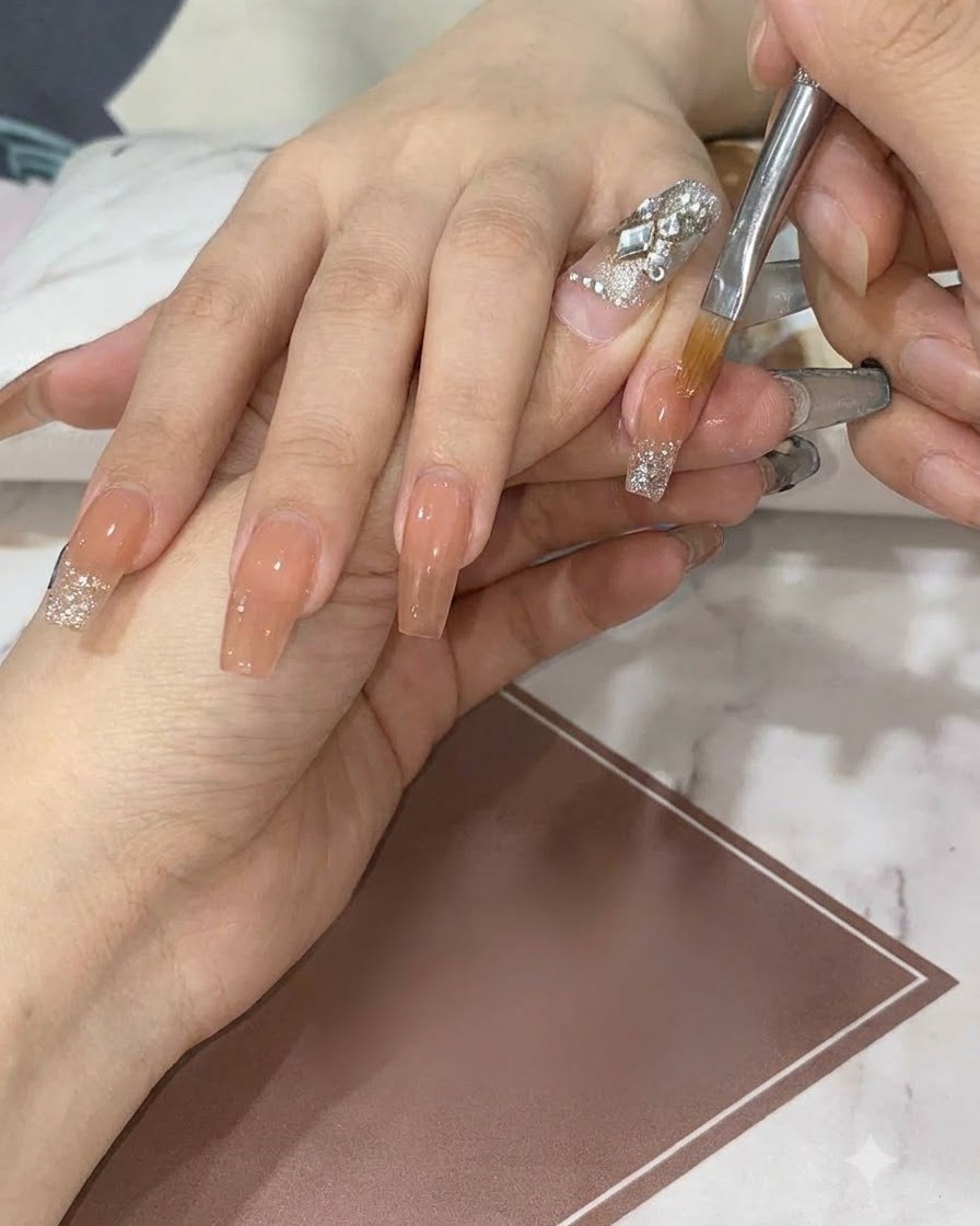 Un pennello piatto di dettaglio sfuma e trascina il glitter argento verso il basso su ununghia nude per creare una sfumatura liscia.
