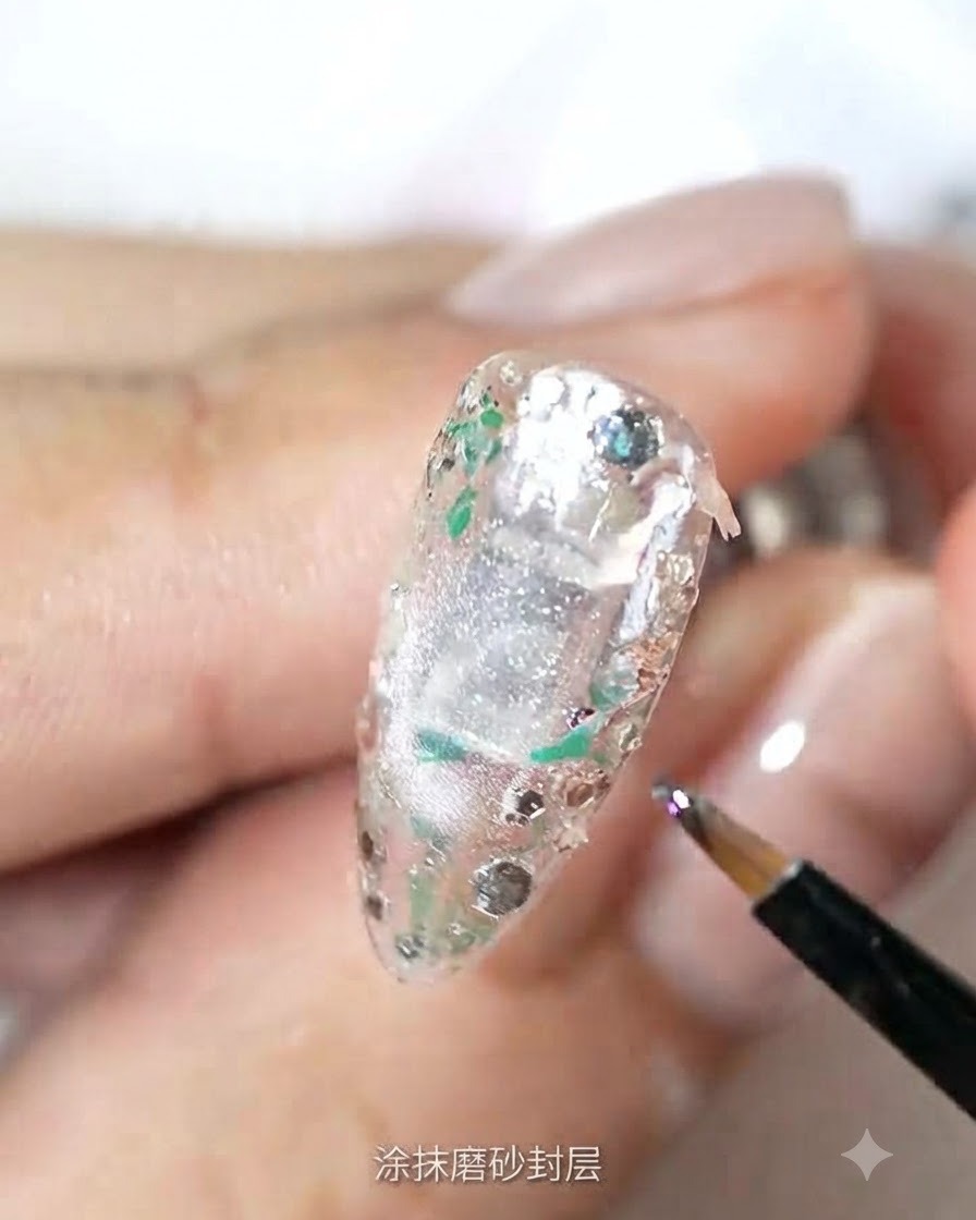 Un pennello sottile applica il top coat opaco su una superficie dellunghia testurizzata e ricoperta di glitter.