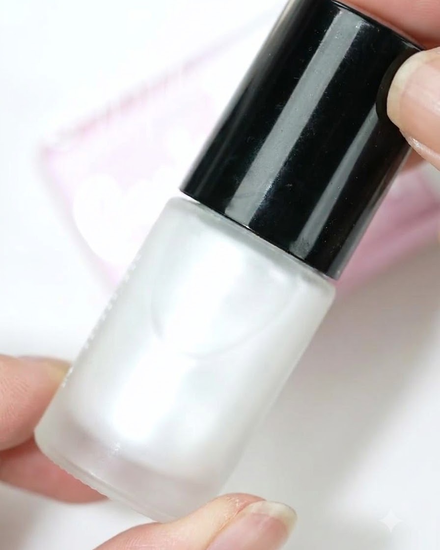 Un flacone di blooming dye bianco perla tenuto contro uno sfondo chiaro.