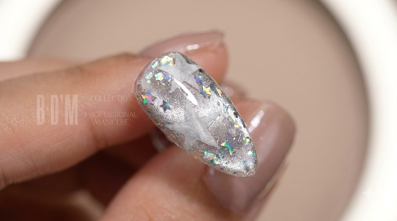Primo piano di unghie finite lucide a mandorla con effetti cat-eye argentati, paillettes a stella olografiche e trasparenti e motivi a stella bianchi stratificati.