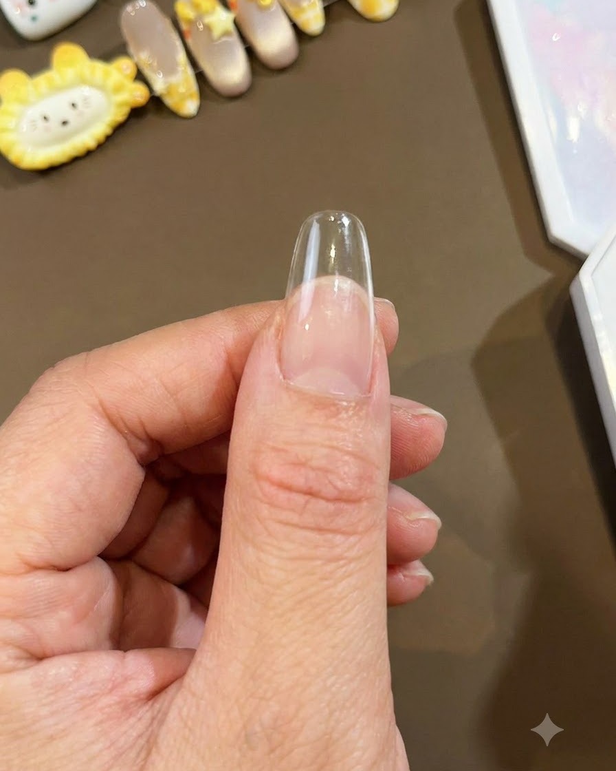 Primo piano di una tip per unghie trasparente e lunga a mandorla tenuta contro un pollice, pronta per lapplicazione della nail art.