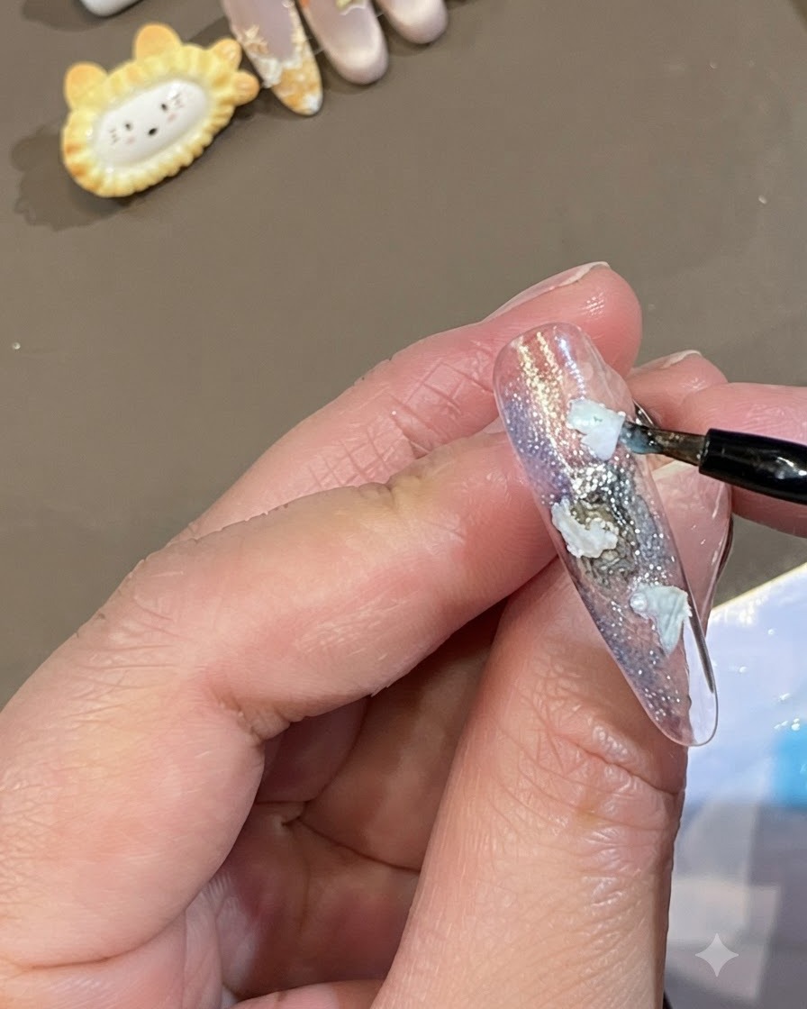Un pennello fine applica puntini di gel blu traslucido attorno ai bordi dei pezzi di conchiglia bianca su ununghia.