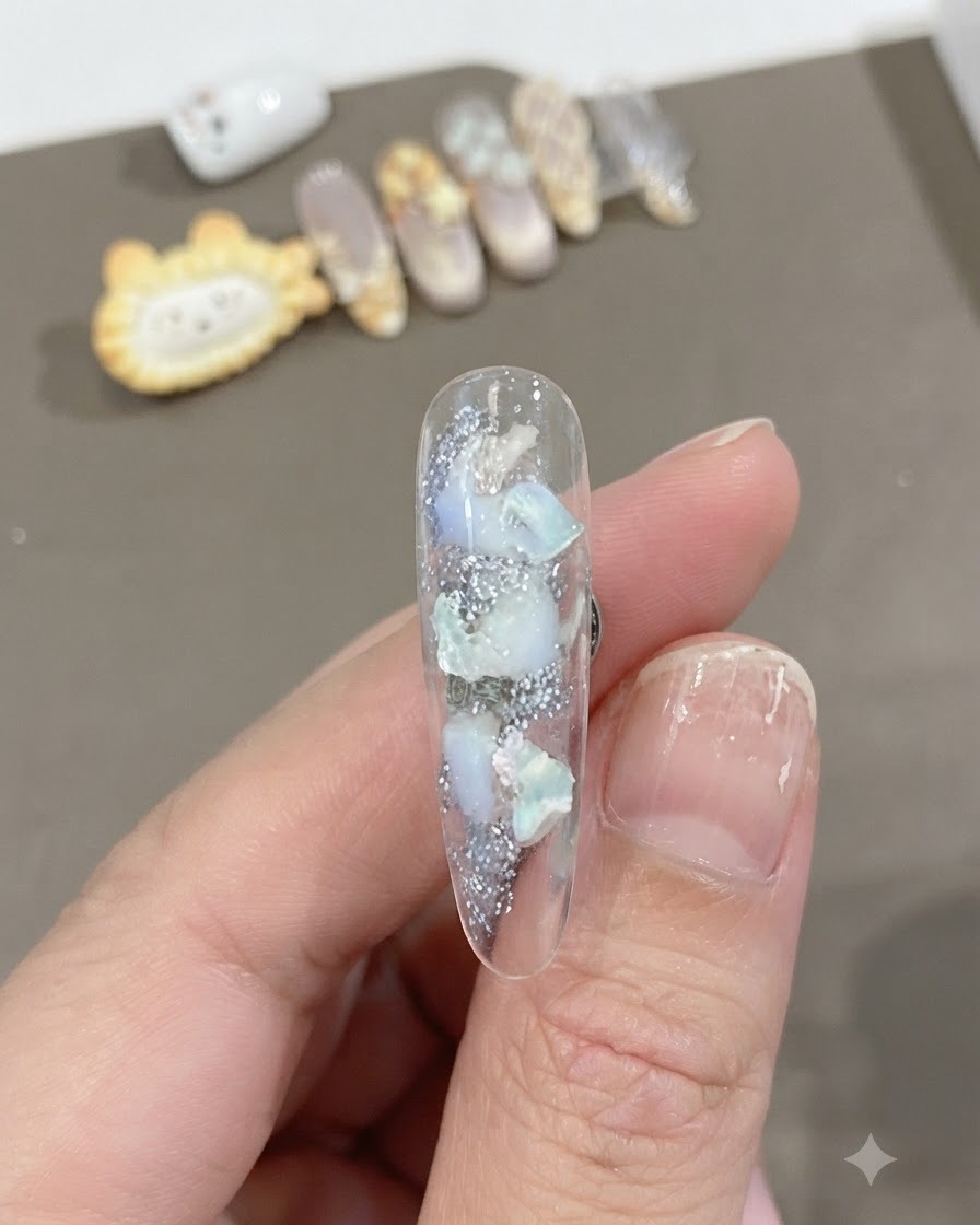 Primo piano di ununghia lunga trasparente con pezzi di conchiglia incorporati e texture brillante con una morbida sfumatura di bianco.